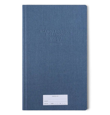 A blue journal has a white "property of" sticker" towards the bottom and in the upper middle of the cover indented into the front cover are Standard Issue Notebook No 17.