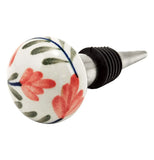 Ceramic bottle stopper end with design of a red flower with green and black stem on a white background attached to a silver colored metal tube with black rubber plug with end facing horizontally towards the front.