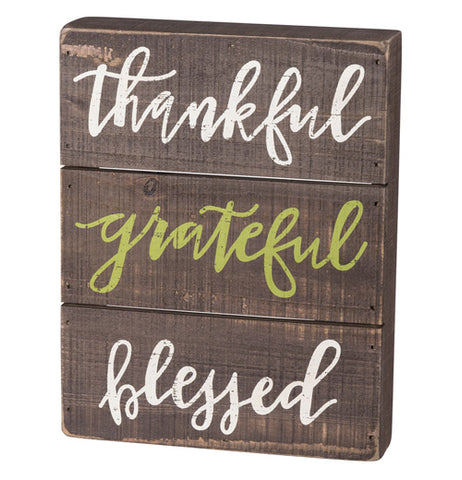 The "Thankful" Slat Box Sign shows the three words, "Thankful, Grateful, Blessed" in white and green cursive letters over a brown wooden background.
