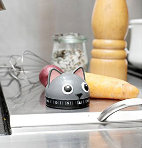 A Cat shape kitchen timer on a counter with a yam and a onion in the background.