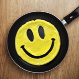 Scrambled eggs shaped to look like a smiling face in a black pan on a brown background.