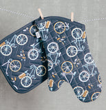 The navy blue oven mitt with white and golden bicycle artwork is hanging on a line next to a potholder with the same color and design.