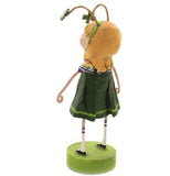 A polyresin figurine of a young, blonde-haired girl. She wears a green and gold painted four-leaf clover headband, a green dress, white socks with two green stripes at the top, and Mary Jane shoes. She is standing angled facing the right, with her back visible.