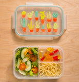 The lunch box with the cactuses on its lid is shown with some vegetables, noodles, and gummy bears in it.