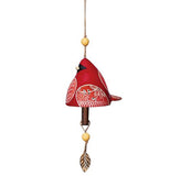 This copper bell has a ceramic bottom that looks like a red cardinal bird with white wings and a white tail. A copper leaf sculpture hangs at the bottom.
