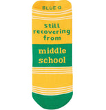 yellow sock with green toes there are white stripes segmenting the sock at the toes about an inch up form the toes and at the top of the sock. the words "Still recovering from middle school" with the middle school part being inside 