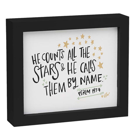 White box sign With gold stars and black frame, print says "He counts all the stars and he calls them by name".