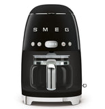 A Black coffee machine with a coffee carafe set up inside it. The base has small "feet" that elevate it slightly. The brand name "Smeg" and buttons are across the body.