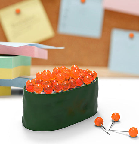 A container shaped as a sushi roll having orange tacks to resemble fish eggs set in an office setting.