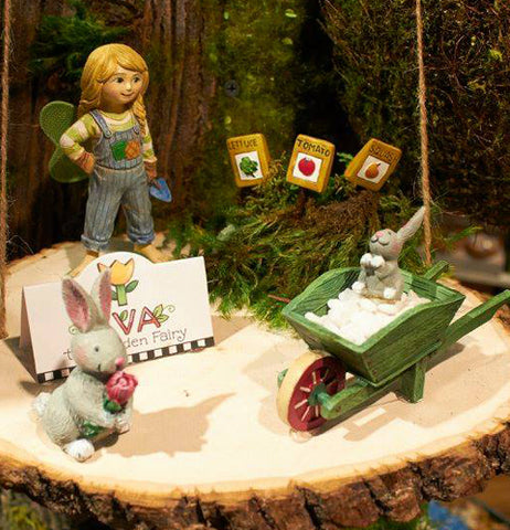 The three (Mini) Garden Pick "Veggie Markers", the squash, the tomato, and the lettuce, are shown in a mini garden along with a fairy girl, a bunny holding a flower and another thats sitting in a green wheelbarrow filled with rice.