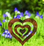 Copper triple heart spinner with chain and hook hanging up in a garden with purple flowers and green grass.