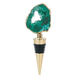 This golden bottle stopper features a teal green gem with a hole in its middle at the top of the stopper.