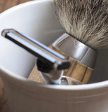 The cup is shown with a brush and shaving razor lying in it.
