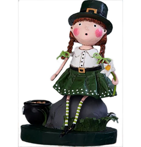A figurine of a rosy-cheeked young girl with brown hair in braids. She's wearing a black top hat with a gold buckle, a white collared shirt, a black belt with gold buckle, a green skirt with white polka dots at the bottom, green and white stripped socks, and black Mary Jane shoes with a gold buckle on them. She sits on a gray rock with green grass to the right of it and a black cauldron with gold coins in it to the left.