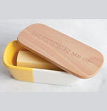 A butter tub 1/3 is yellow and rest is white with a wooden lid that says "Butter me up".
