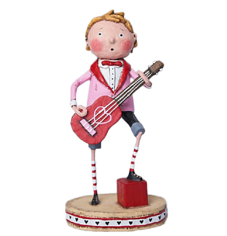 A resin figurine of a blonde man holding a red and pink guitar standing on a light brown base. The guitar has a heart decal in the middle. The man is wearing a pastel pink, white, and red suit, black and gray shorts, red and white striped socks, and black shoes. He is putting one foot on a red block. Red and white stripes on the outside edge of the base have black hearts in the middle.