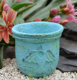 The (Mini) Blue Bird Planter has the symbol of a bird and sits outside the garden on a gravel. 