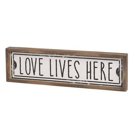 The "Lives Here" Street Sign features the message that reads, "Love Lives Here" in black over a white background surrounded by rectangular brown wooden frame.