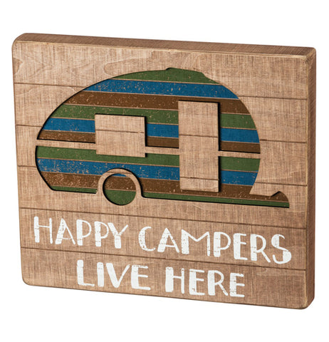 This sign "Happy Campers Live Here" painted white on tanned wood below the green, red, and blue striped camper. 