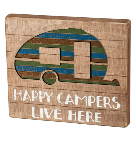 This sign "Happy Campers Live Here" painted white on tanned wood below the green, red, and blue striped camper.