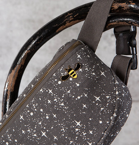 An enamel pin of a black and yellow honeybee attached to a black fanny pack with a white star design.
