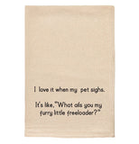 A beige tea towel with black text reading "I love it when my pet sighs. It's like 'What ails you my furry little freeloader?'"