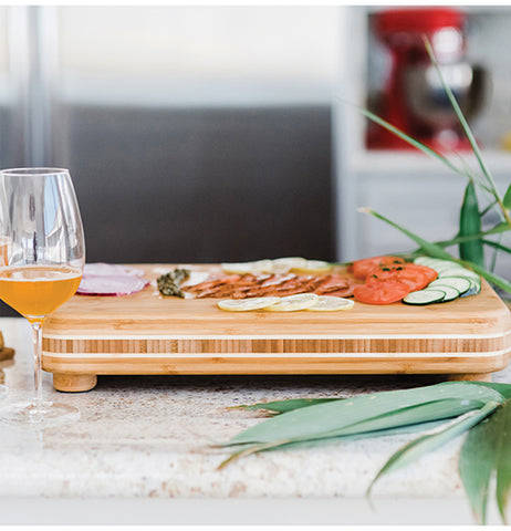 A wodden cutting board being used to display vegetables. It has sliced onions, tomatos, lemons, and cucumbers.