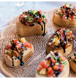 A wooden cutting board is being used to display several bread snacks with a vegetable topping.