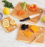 Three wooden light brown/yellow cutting boards are being used. They are all different sizes. The smallest has cut up lemons. The medium sized one has cut up cheese, uncut olives, and a cheese knife on it. The biggest has uncut celery, a cut up pepper bell pepper, and a knife. Lemons and a blue plate surround the cutting boards.