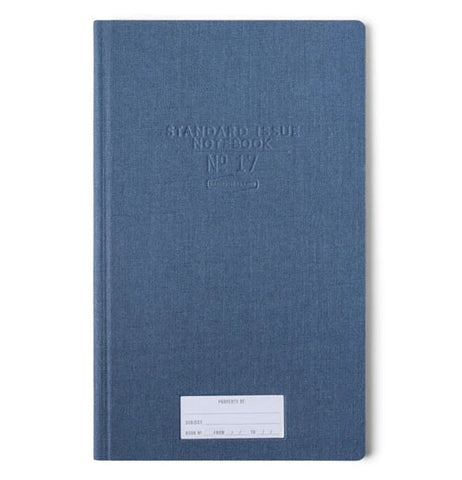 A blue journal has a white "property of" sticker" towards the bottom and in the upper middle of the cover indented into the front cover are Standard Issue Notebook No 17.