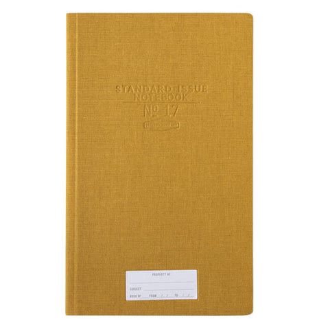 A mustard yellow journal has a white "property of" sticker" towards the bottom and in the upper middle of the cover indented into the front cover are Standard Issue Notebook No 17.