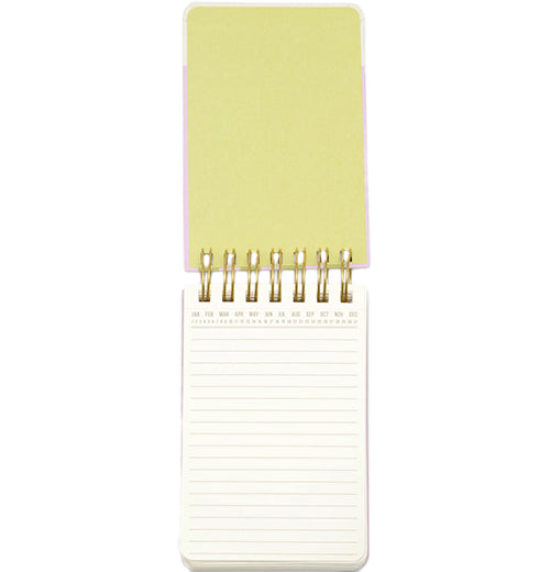 A wired pocket notebook opens vertically to reveal white lined pages and a pastel green front cover.