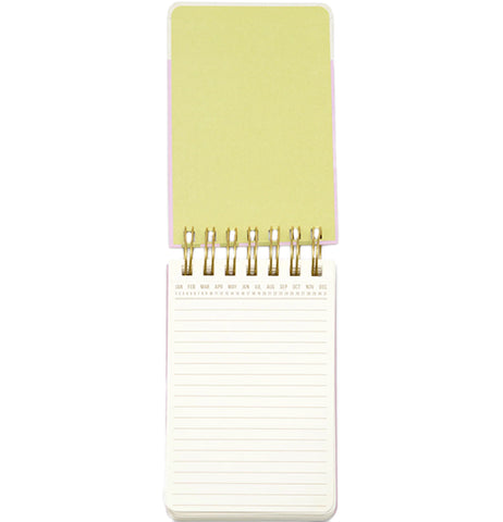 A wired pocket notebook opens vertically to reveal white lined pages and a pastel green front cover.