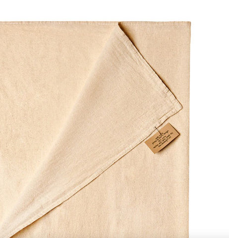 Folded corner of the kitchen towel that shows both front and back of the dish towel at the same time with a tag attached to the edge with the care instructions on it.