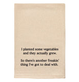 A beige tea towel with black text reading "I planted some vegetables and they actually grew. So there's another freakin' thing I've got to deal with."