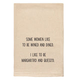 A beige tea towel with black text reading "Some women like to be wined and dined. I like to be margarita'd and queso'd."