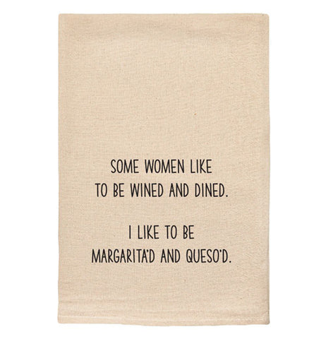 A beige tea towel with black text reading "Some women like to be wined and dined. I like to be margarita'd and queso'd."