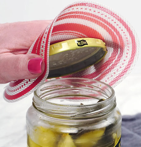 A white and red jar opener is being used by a disembodied caucasion hand to open a jar of olives.