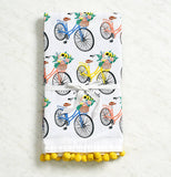 The white towel with the different colored bikes carrying baskets of flowers is shown against a creamy white background.