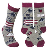 A Pair of the "Go Away I'm Reading" socks are crossed in order to show the full design of the books under a book lamp and the text "Go Away". A single version of the sock is standing up showing what it would like fitted over a foot. 