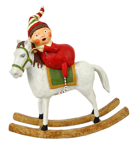 A young girl is riding a white rocking horse with a green halter and green and brown saddle pad. She wears a white, red, and green stocking cap, with red and white pajamas and socks.