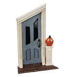 A blue asymmetric door with white framing and an orange jack o lantern on a pedesta