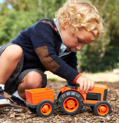 A boy playing the orange truck on the ground. 