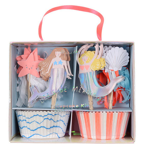 The "Let's Be Mermaids" Cupcake Kit box has 2 sets of wrappers in 2 styles one is white with blue waves, the other features pink and white vertical stripes with with 4 styles of cupcake toppers, two mermaids one is brunette and one is blond and two styles of seashells. 