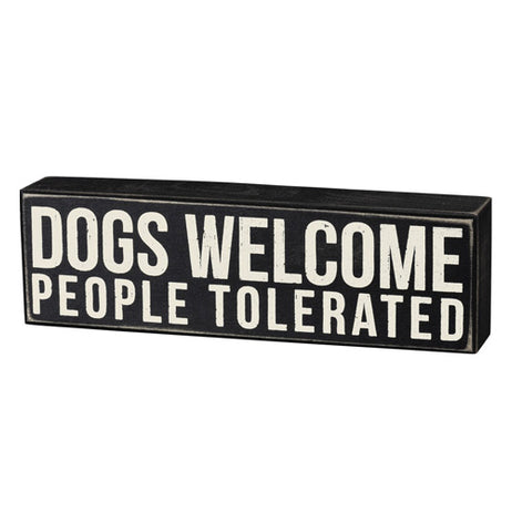 This rectangular-shaped box sign has white letters on a black background that read, "Dogs Welcome People Tolerated".