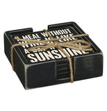 This black wooden holder contains a set of five black wooden coasters, the top of which reads in white lettering, "A Meal Without Wine is Like a Day Without Sunshine".