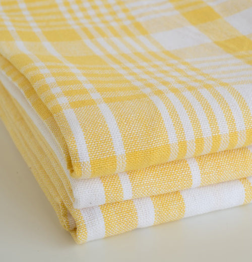 Three bright yellow lemon dish towels two striped and one plaid sitting on a counter. on a counter.