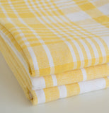 Three bright yellow lemon dish towels two striped and one plaid sitting on a counter. on a counter.