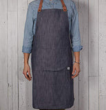 Someone wearing the Denim renew apron that has the adjustable leather neck strap.