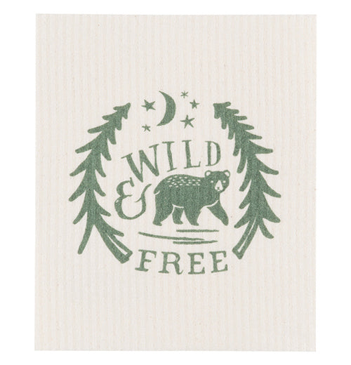 This cream colored dishcloth features a green design of a bear walking between two trees under stars and a moon. The words, "Wild &amp; Free" are shown above and below the bear in green lettering.